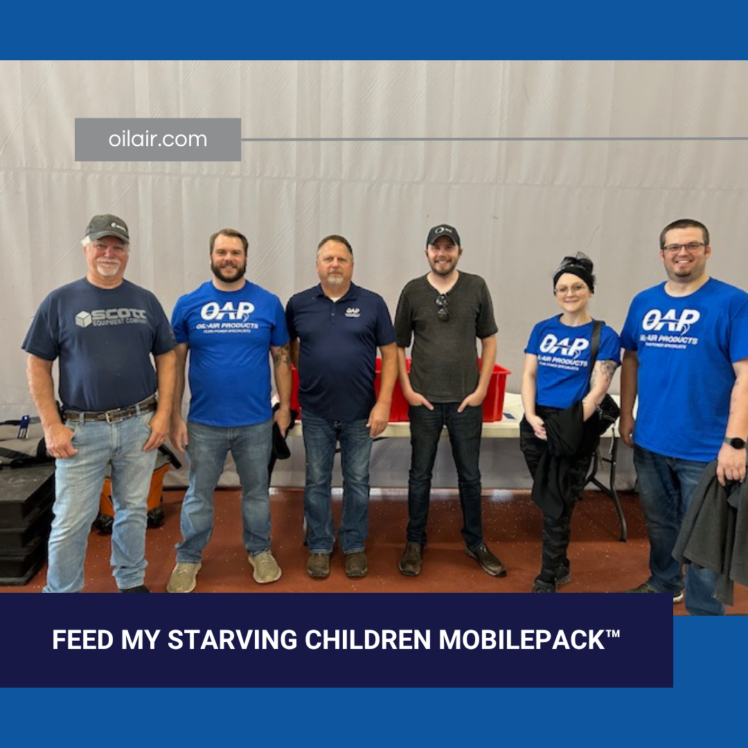Six team members, four wearing OAP shirts, stand in front of a Feed My Starving Children food packing station